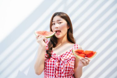 Kırmızı elbiseli güzel Asyalı kadın elinde bir parça karpuz tutuyor. Güzel Asyalı kadın bir parça karpuz yemekten hoşlanıyor. Beyaz arkaplan.