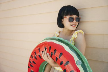 Bob saç kesimi, sarı kolsuz bluz ve güneş gözlüğü takan güzel Asyalı kadın can simidiyle poz veriyor ya da yüzüyor..