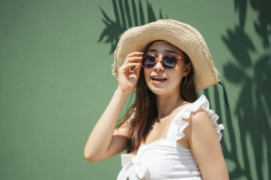 Yeşil arka planda şapka ve güneş gözlüğü takan güzel bir kadının portresi. Plajda yaz tatili.