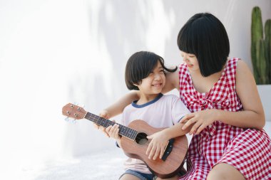 Tatlı Asyalı kız kardeşi küçük kardeşine odada gitar çalmayı öğretiyor. Müzik aleti öğretiyorum..