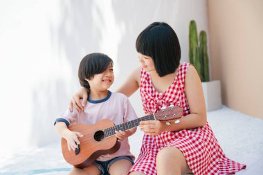 Tatlı Asyalı kız kardeşi küçük kardeşine odada gitar çalmayı öğretiyor. Müzik aleti öğretiyorum..