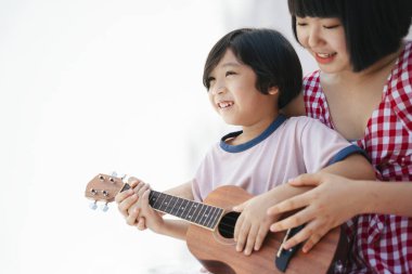 Tatlı Asyalı kız kardeşi küçük kardeşine odada gitar çalmayı öğretiyor. Müzik aleti öğretiyorum..