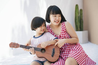 Tatlı Asyalı kız kardeşi küçük kardeşine odada gitar çalmayı öğretiyor. Müzik aleti öğretiyorum..