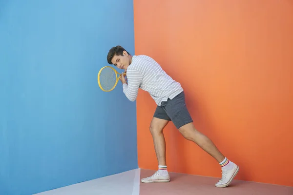 迷人的年轻亚洲男子穿着休闲装 手握网球拍 背景为蓝色橙色 很有趣的姿势打网球 准备好了球的姿势 — 图库照片