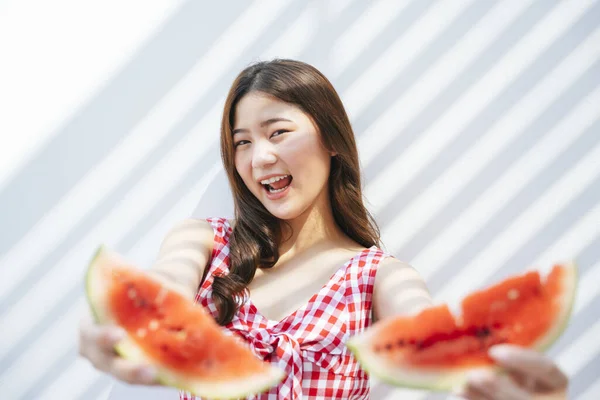 背景に新鮮なスイカを食べる赤いドレスを着たアジアの若い女性 幸せな女性と果物の一片 — ストック写真
