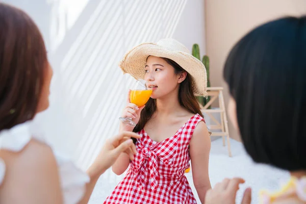 美しい若いですアジアの女性身に着けている帽子と赤いドレス飲みオレンジジュースとともに友人で夏パーティー — ストック写真