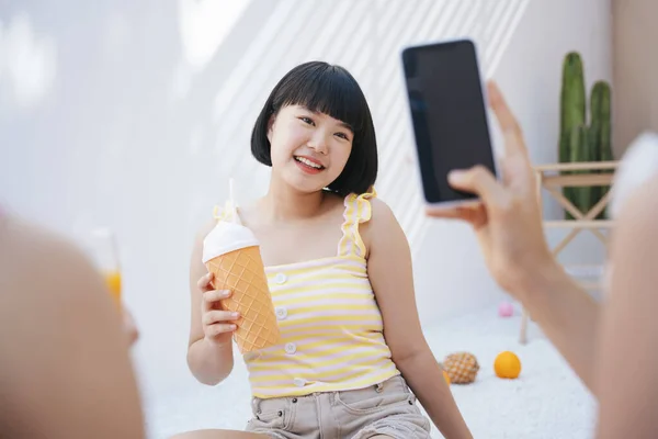 Cute young asian bob hairstyle woman holding plastic cup. Friend taking picture with smartphone. Summer party.