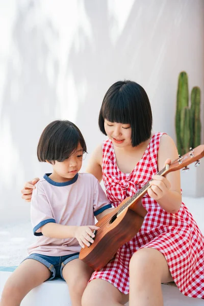 Cute Asian Sister Teaching Her Little Brother How Play Ukulele Royalty Free Stock Images