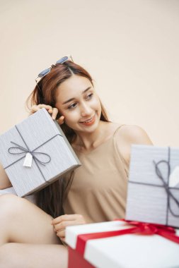 Güzel bir kadın hediye kutusunda oturuyor. Mutlu yüz ve kendine güvenen gülümseme. Bej krem arka planda izole edilmiş..