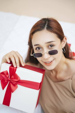 Güneş gözlüğü takan güzel bir kadın beyaz koltukta hediye kutusunda oturuyor. Hediye kutusu ve genç güzel kız..