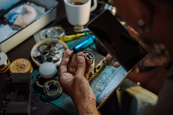 A man fix the film camera and clean the dust on the lens then assemble all the part together, look at the cleaning tutorial on internet by smartphone.