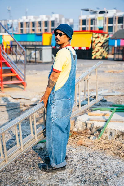 Man Yellow Shirt Denim Overalls Standing Abandoned Amusement Park Sunny — Stock Photo, Image