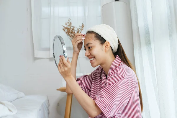 Kırmızı pijamalı ve bantlı uzun saçlı kadın sabah yüzünü silerken yerde oturuyor..