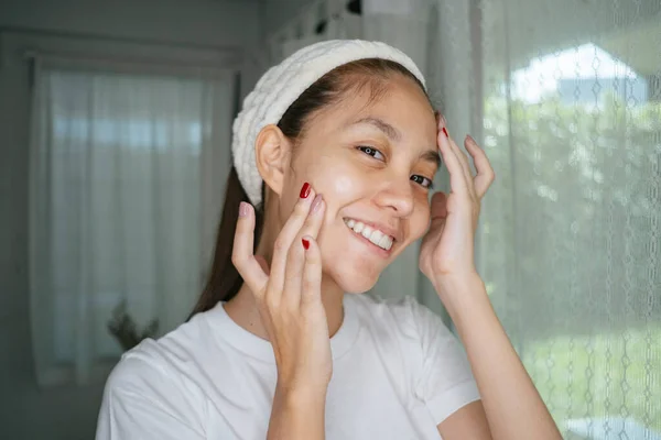 Woman with nail painting in white t-shirt and headband apply facial cream on her face.