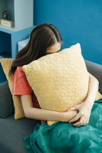 Long hair woman sitting on sofa in living room with green blanket hug yellow pillow while her online store can\'t make the profit, more over the store is in the red.