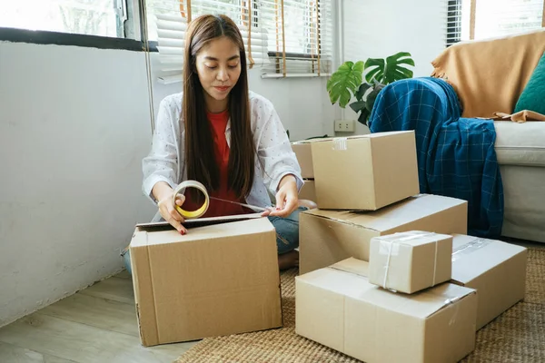 Long hair woman packing a product of her online shop to send it to customer.