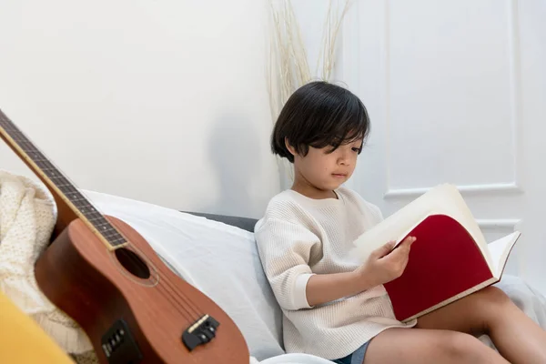 Lindo Niño Leyendo Cuento Libro Sentado Sofá Con Ukulele Sala —  Fotos de Stock