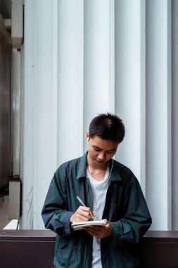 Kısa saçlı adam işi için bir fikir düşünüyor ve iş yerinin dışındayken defterine not alıyor..