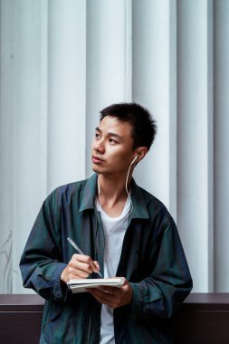 Kısa saçlı adam işi için bir fikir düşünüyor ve iş yerinin dışındayken defterine not alıyor..