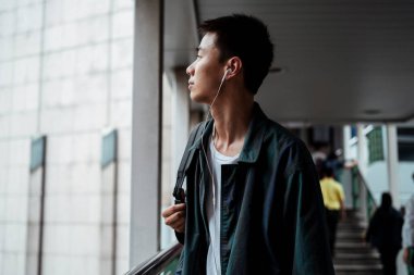 Kısa saçlı adam kulağında kulaklıkla alışveriş merkezinden gökyüzüne doğru yürüyor..