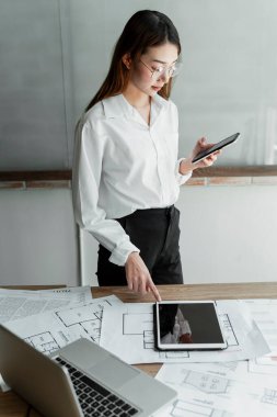 Tablette önceki tasarımı bulmak için beyaz gömlekli, gözlüklü, uzun saçlı kadın iç mimar Tyr..