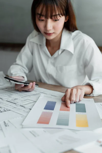 Long hair designer woman in white shirt look at the color on the palette paper and compare with the palette in smartphone