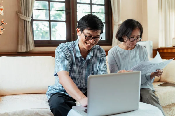 The difference between old fashion way and new fashion way. Grandfather reading news on the internet using laptop. Grandmother reading newspaper for information this morning. Elderly parents received information in difference way.