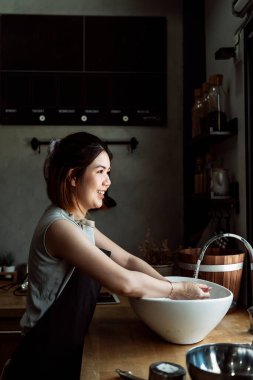 Neşeli Asyalı kadın mutfakta yemek pişirmeden önce lavaboda ellerini yıkıyor..