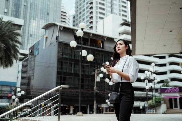 Beyaz Tişörtlü Asyalı Kadını Akıllı Telefon Kullanarak Şehirde Yürüyor — Stok fotoğraf