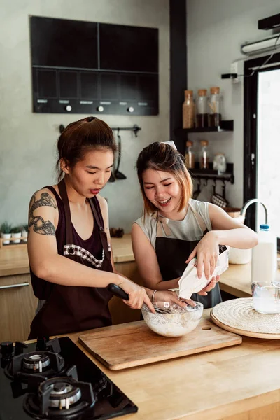 Two asian baker woman mixing flour, milk, egg yolk in glass bowl together in kitchen. Making bread procedure.