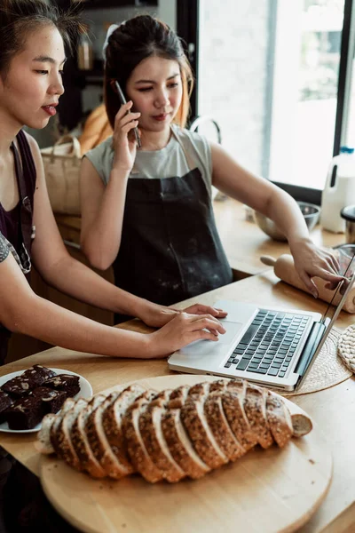 stock image Two bakery chef searching for ingredients on laptop and order right away with smartphone.