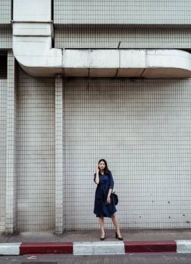 Mavi elbiseli güzel Asyalı kadın beyaz duvardaki patikaya seksi bir şekilde bakıyor..