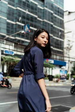 Büyük şehirde yolda yürüyen mavi elbiseli güzel Asyalı bir kadının arka manzarası..