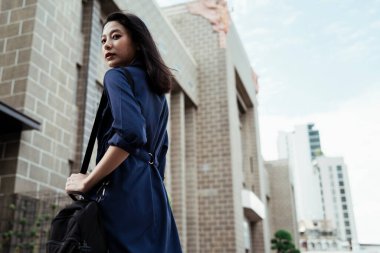 Arka plan - mavi elbiseli güzel Asyalı kadın siyah çanta taşıyor Bangkok 'ta seyahat ediyor.