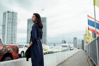 Rüzgarlı bir günde mavi elbiseli güzel Asyalı bir kadının sokakta dikilirken yan görüntüsü..