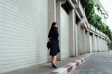 Mavi elbiseli, siyah çantalı güzel bir Asyalı kadın şehrin kaldırımında yürüyor..