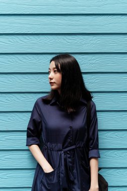 Mavi elbiseli güzel Asyalı bir kadının portresi mavi ahşap duvar arkasında duruyor..