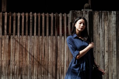 Kırsal ahşap duvarda, eski semtte ve eski evde mavi elbiseli güzel Asyalı bir kadın..