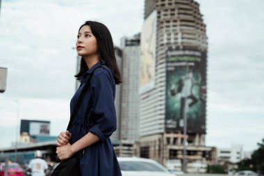 Mavi elbiseli güzel genç Asyalı kadın caddede duran gökyüzüne bakıyor..