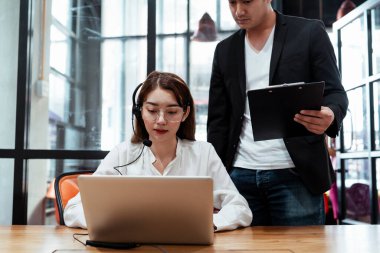 Genç Asyalı bayan çağrı merkezi servisi olarak işe girdi. Mikrofon takıp müşteriyle konuştu. Bilgi almak için dizüstü bilgisayarda yazdı. Denetmen, ona yakın durup nasıl çalıştığına dair her şeyi öğretiyor. Stajyer.