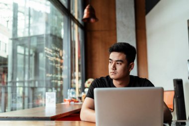 Diz üstü bilgisayarda çalışan, evine bakan yetişkin bir Taylandlı..