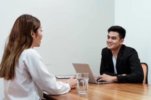 Employer or recruiter reading a resume on laptop during questioning young asian lady at job interview. Young asian woman explaining about her profile to business manager sitting in job interview.