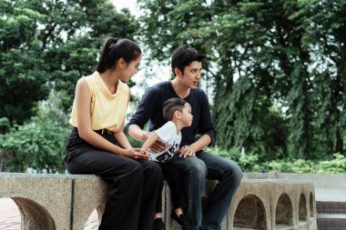 Baba, anne ve oğul hafta sonu parktaki kaldırım taşı bankında oturuyorlar..