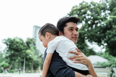Siyah tişörtlü bekar bir baba hafta sonu parkta seyahat ederken oğlunu taşıyor..