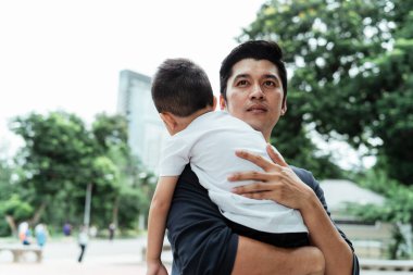 Siyah tişörtlü bekar bir baba hafta sonu parkta seyahat ederken oğlunu taşıyor..