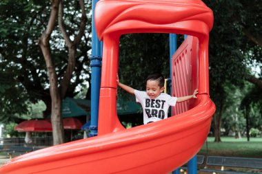 Beyaz tişörtlü küçük bir çocuk parktaki oyun parkının keyfini çıkarıyor..