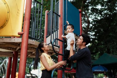 Babam ve annem, o parkın oyun parkındaki oyuncağa tırmanırken oğullarına destek oluyor..