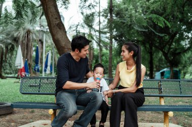 Küçük çocuk yorgun, ailesiyle bankta oturuyor ve su içiyor..