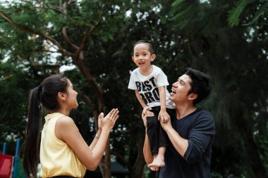 Parkta mutlu bir aile zamanı, baba oğlunu kucağında tutarken anne onu taşımak istiyor..
