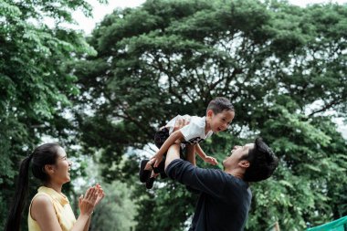 Küçük bir çocuk, bir baba onu kucağına aldığında ve bir anne gülerken kafasını uçak gibi kaldırdığında eğlenir..